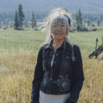 Photo of Dawn Morrison, she's wearing sunglasses and a jeans jacket, with a green field behind her