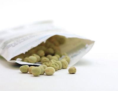 Green pea seeds spill out of an open paper packet on a white table